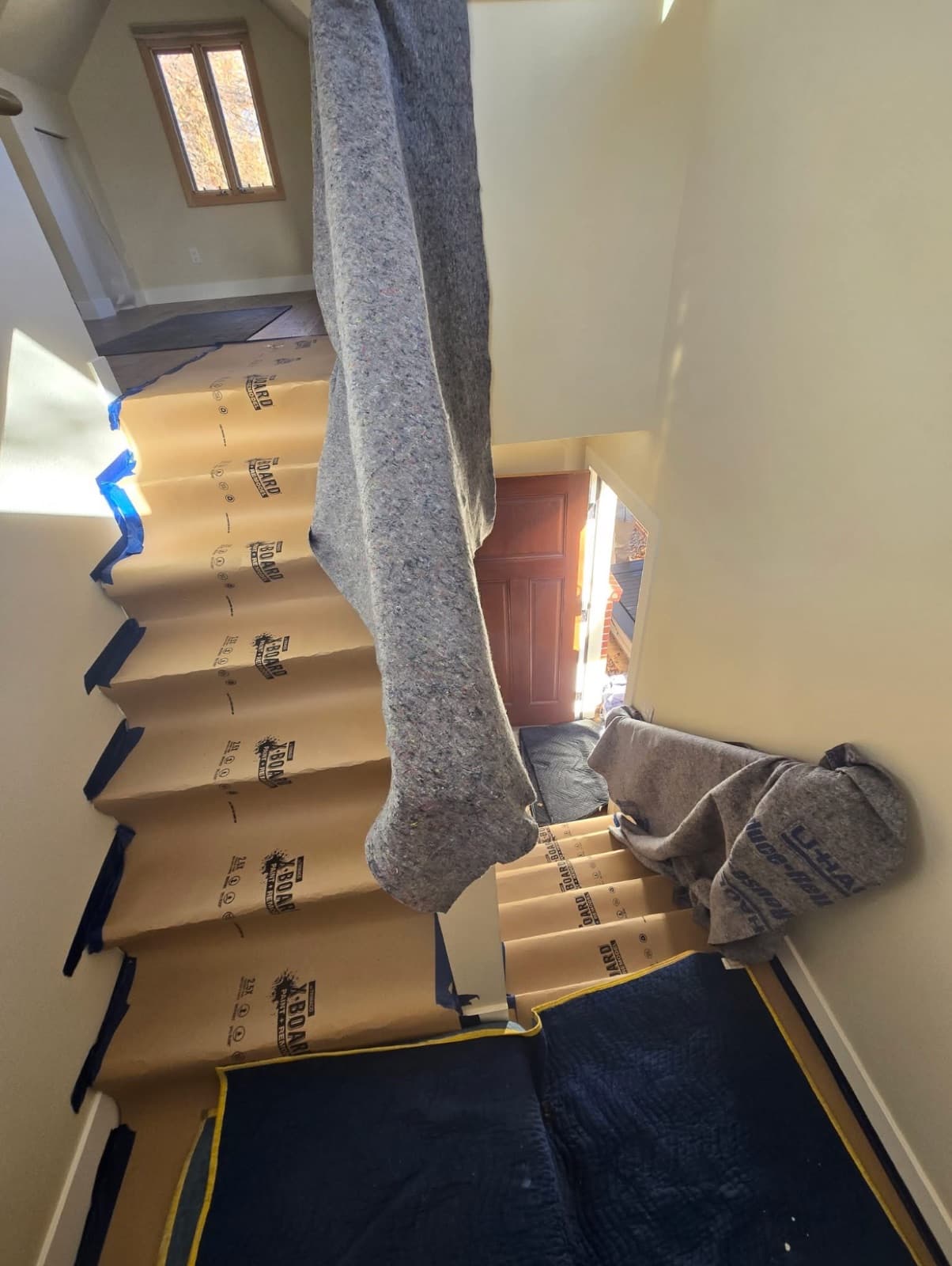 Staircase covered with cardboard runners and blue painter's tape to protect floors and walls during a move